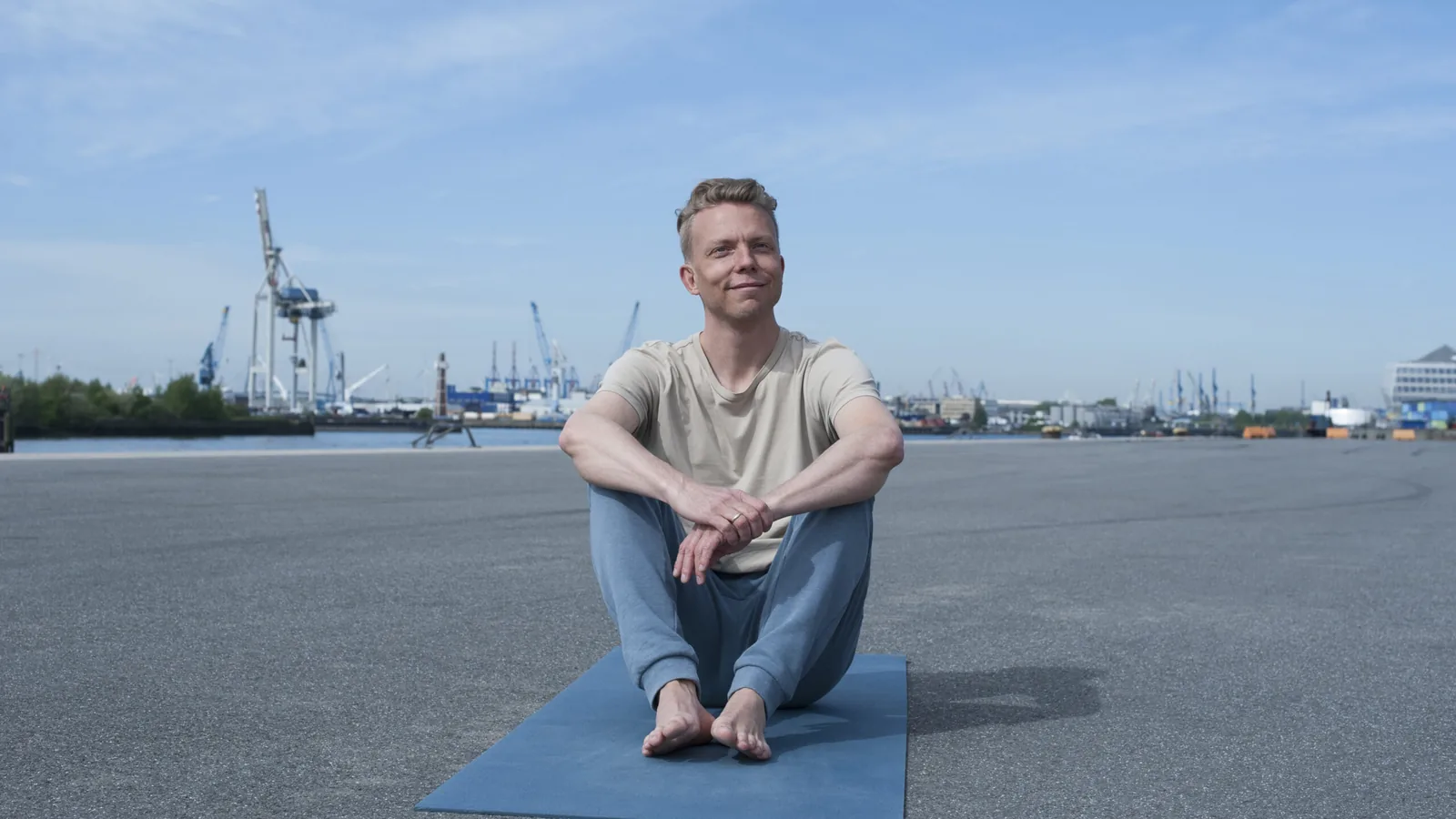 Jan Wolk, Inhaber von Somatic Web, sitzt auf einer Yogamatte vor der Hamburger Hafenkulisse